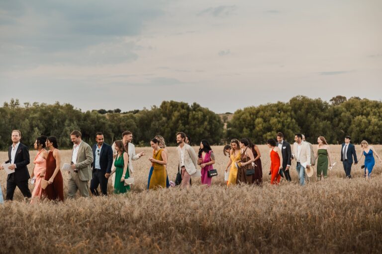 Guests in colour walking in single file through ripe wheat, Pangiunìa Wedding