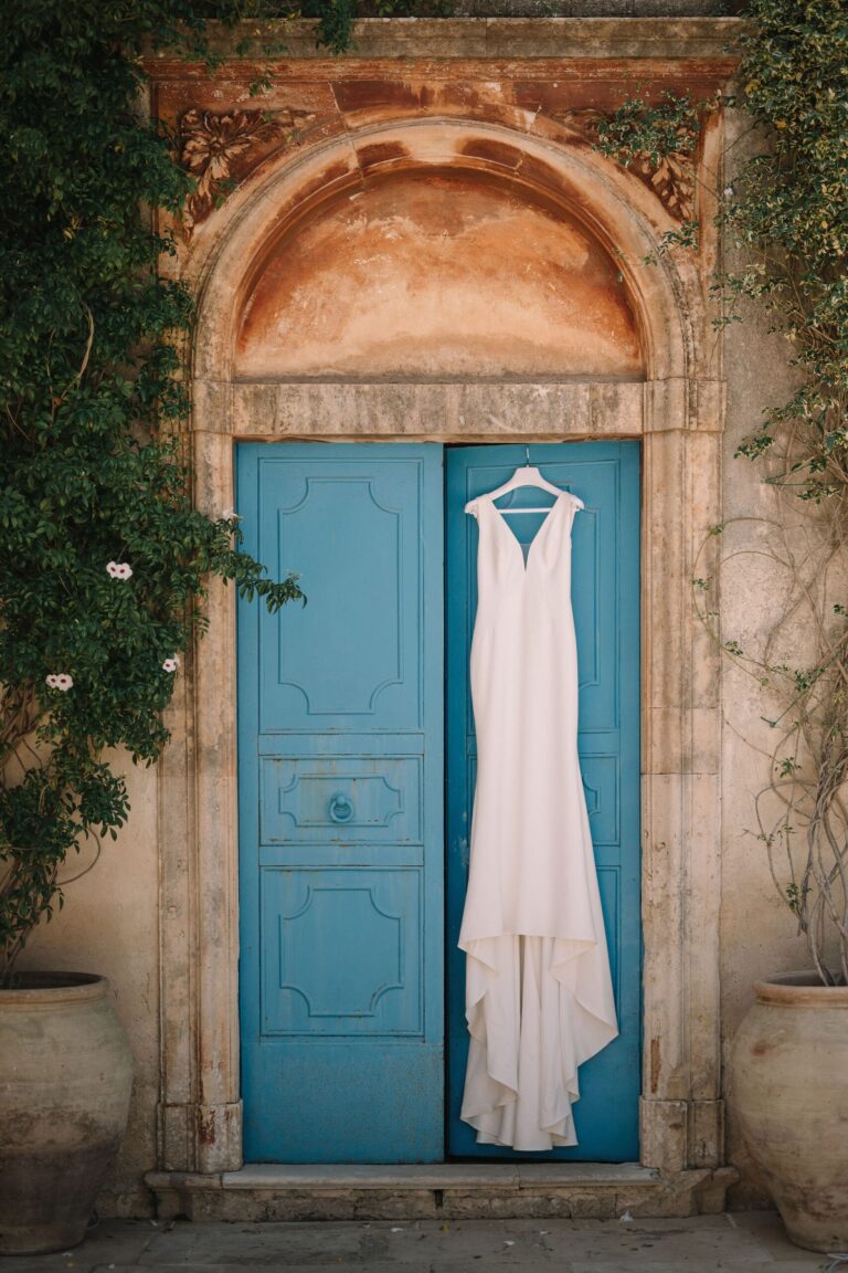 The dress hanging on a bright blue door in a carved stone surround, Pangiunìa Wedding