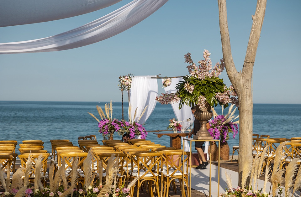 A seaside ceremony set-up with a draped canopy and floral arrangements