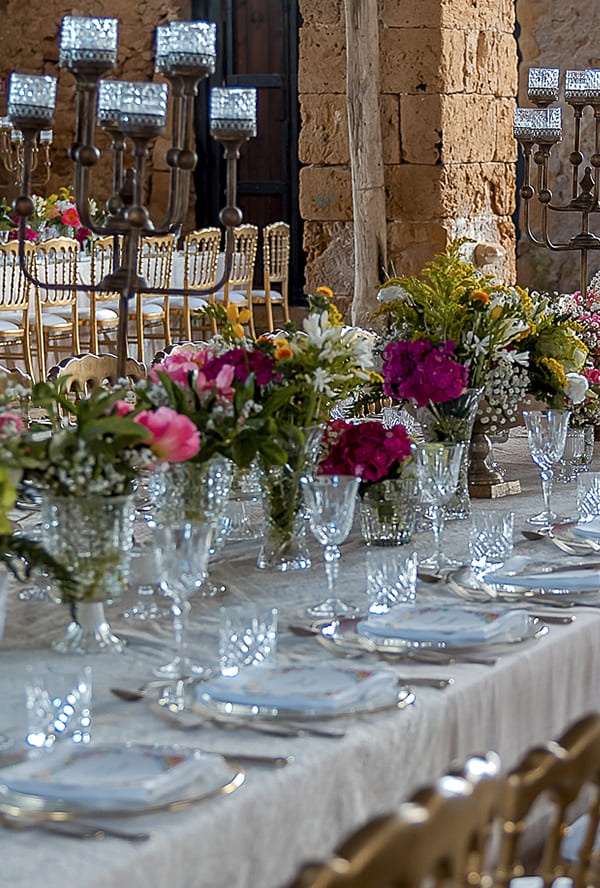 A long table with candlesticks and mixed flowers inside a historic tonnara