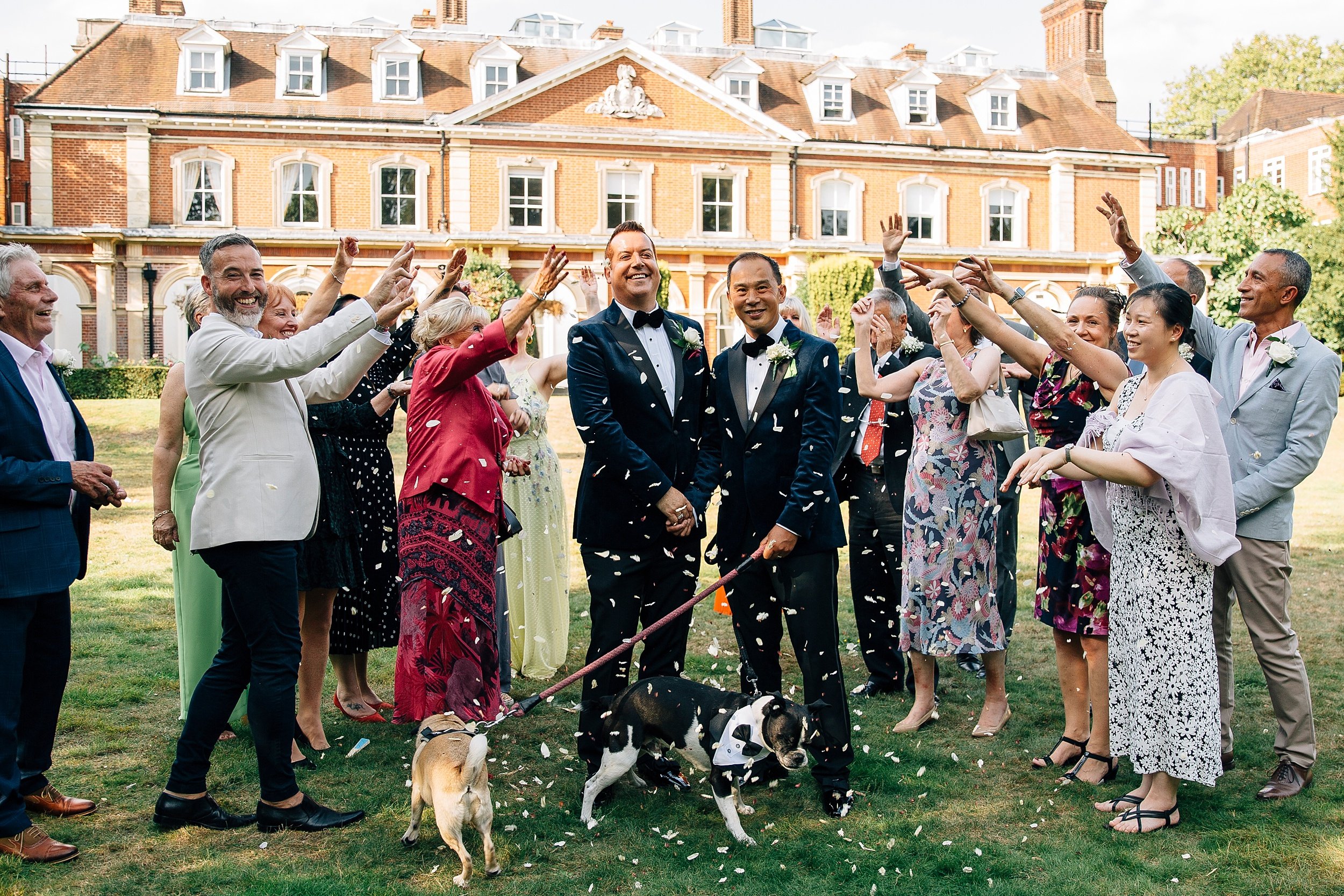 Two grooms, their guests and their two dogs under a shower of confetti on the lawn, Paola De Paola Photography