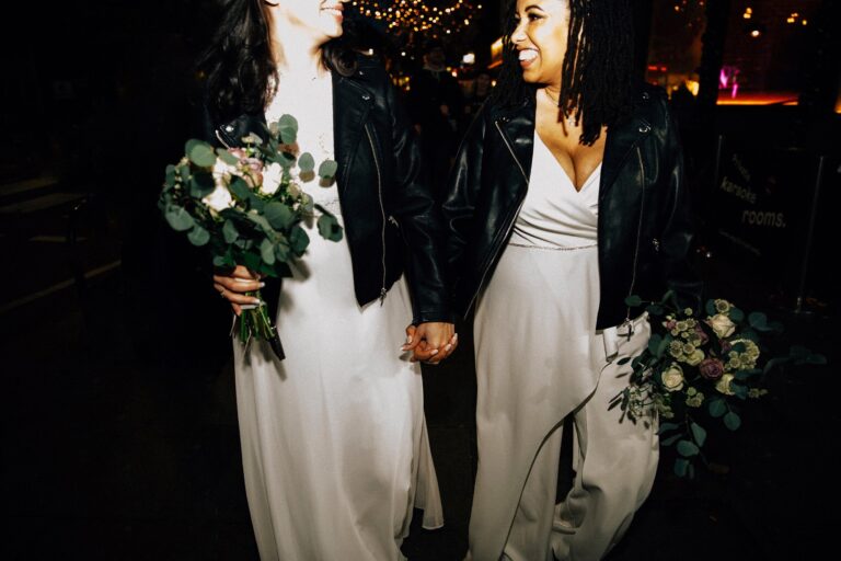 Two brides in leather jackets, hand in hand, at their evening party, Paola De Paola Photography