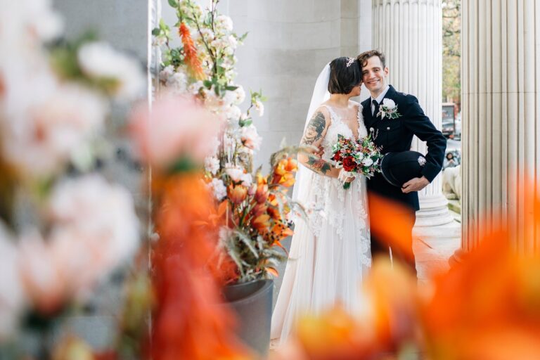 A bride and groom framed by orange flowers between stone columns, Paola De Paola Photography