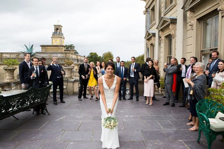 A bride with her bouquet on the terrace at Cliveden House, guests gathered around, Paola De Paola Photography