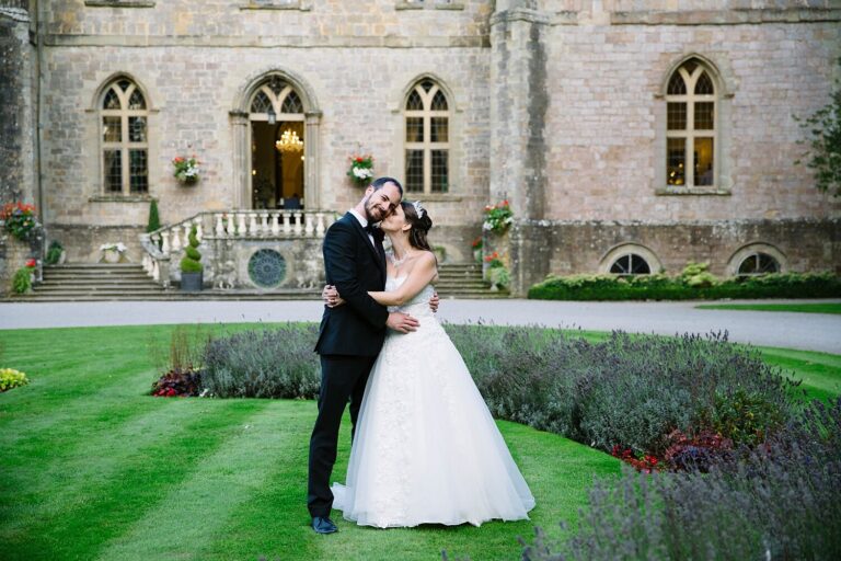 A bride and groom embrace on the lawn in front of Clearwell Castle in the Forest of Dean, Paola De Paola Photography