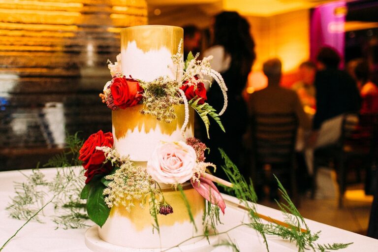 A gold-leaf wedding cake with red and blush roses at The Roseate, Reading, Paola De Paola Photography