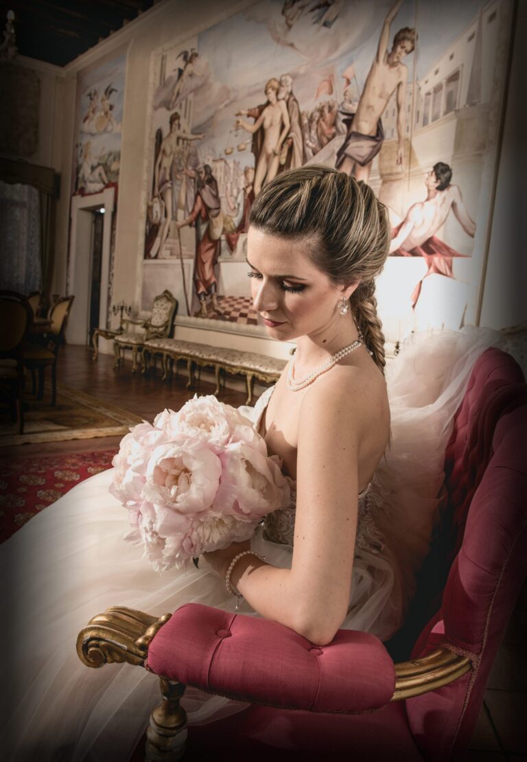 Bride with a loose braid and peony bouquet seated on a velvet chair in a frescoed room, Paola Giancola Makeup