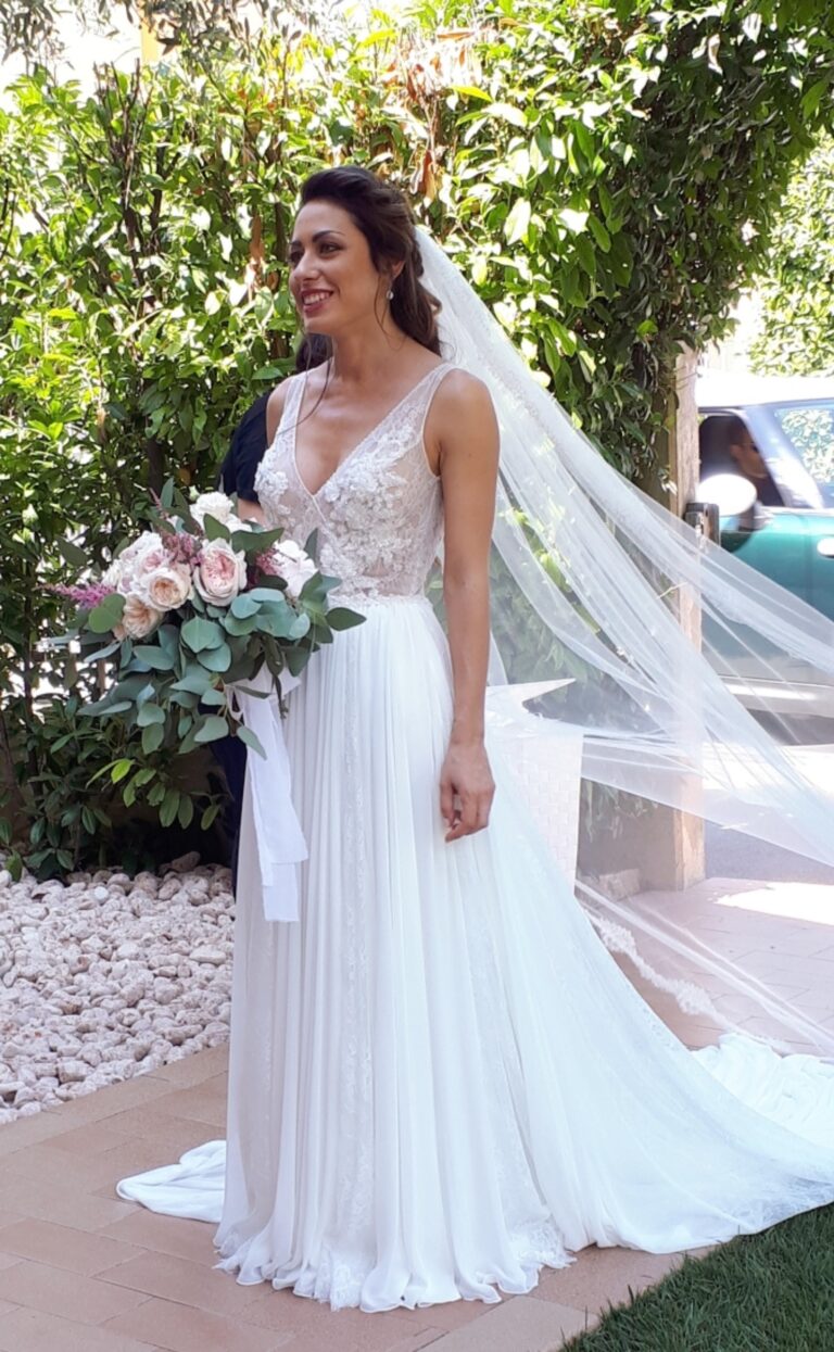 Bride in a long veil and floaty gown holding a bouquet in a garden, Paola Giancola Makeup