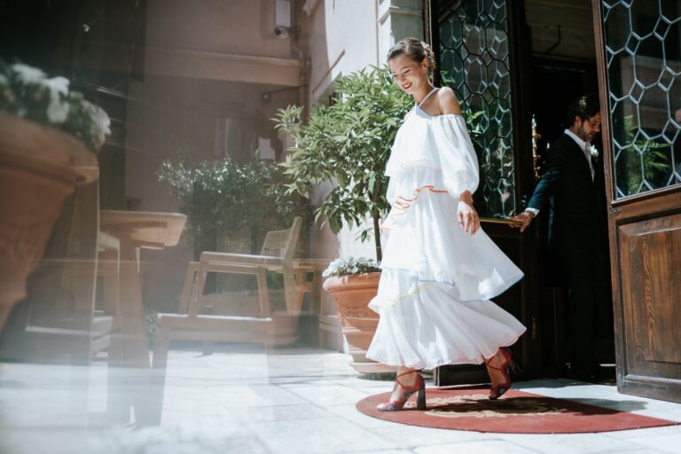Bride in a white tiered dress stepping through a doorway in Venice, Paola Giancola Makeup