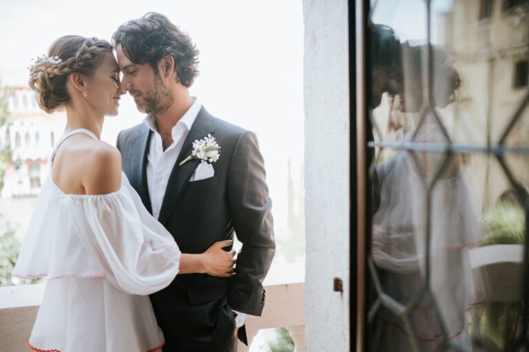 Couple embracing on a balcony with a bridal updo in the foreground, Paola Giancola Makeup