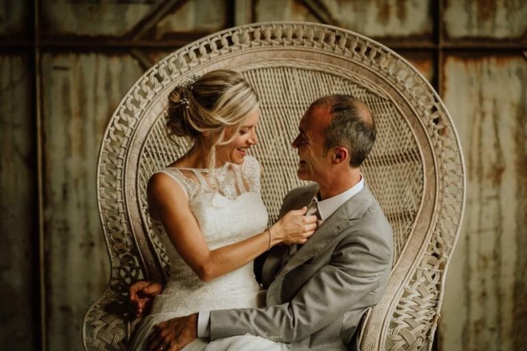Bride in a lace dress seated beside her father in a wicker chair, Paola Giancola Makeup