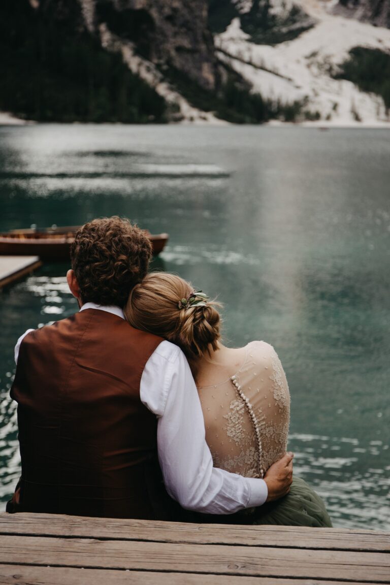 Couple sitting together on a lake jetty, the bride with a braided updo, Paola Giancola Makeup