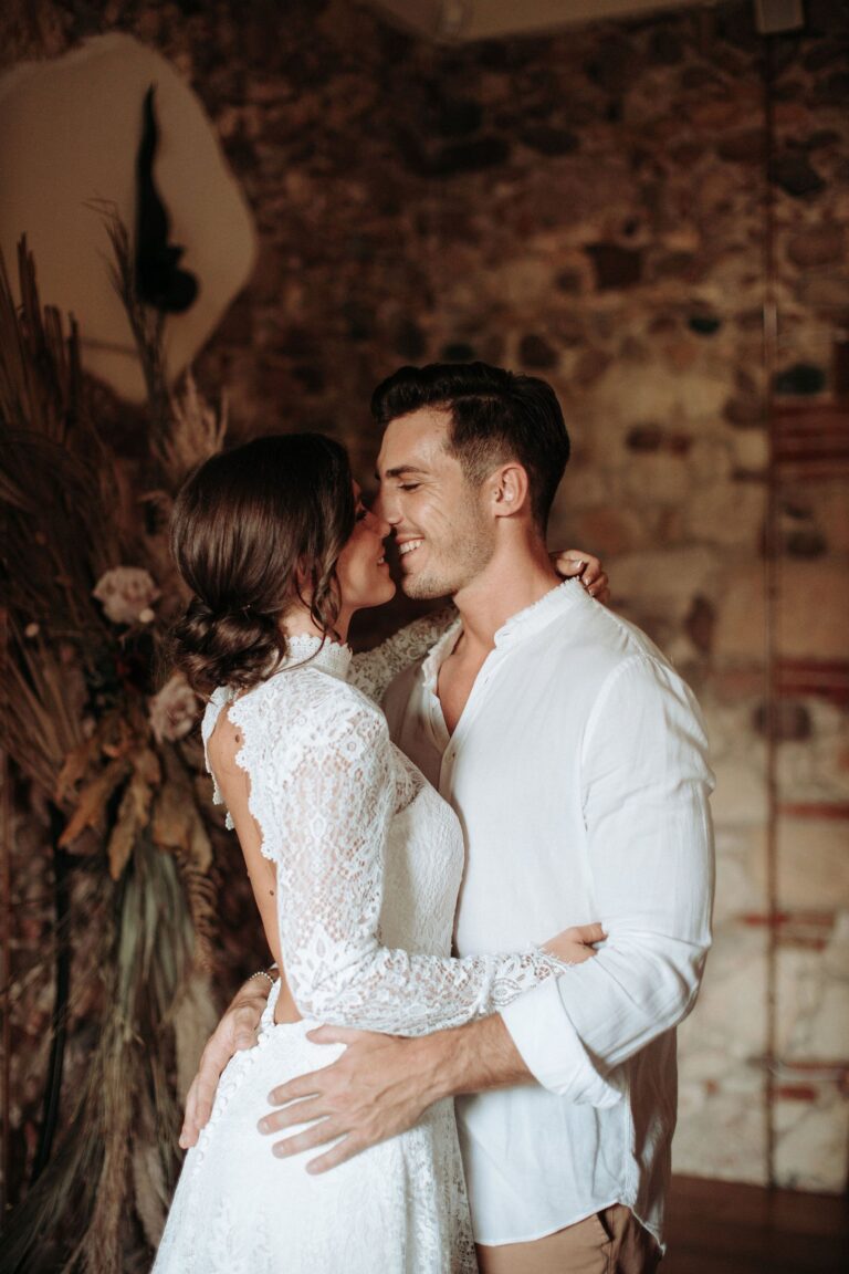 Couple in an embrace in a rustic stone interior with dried flowers, Paola Giancola Makeup