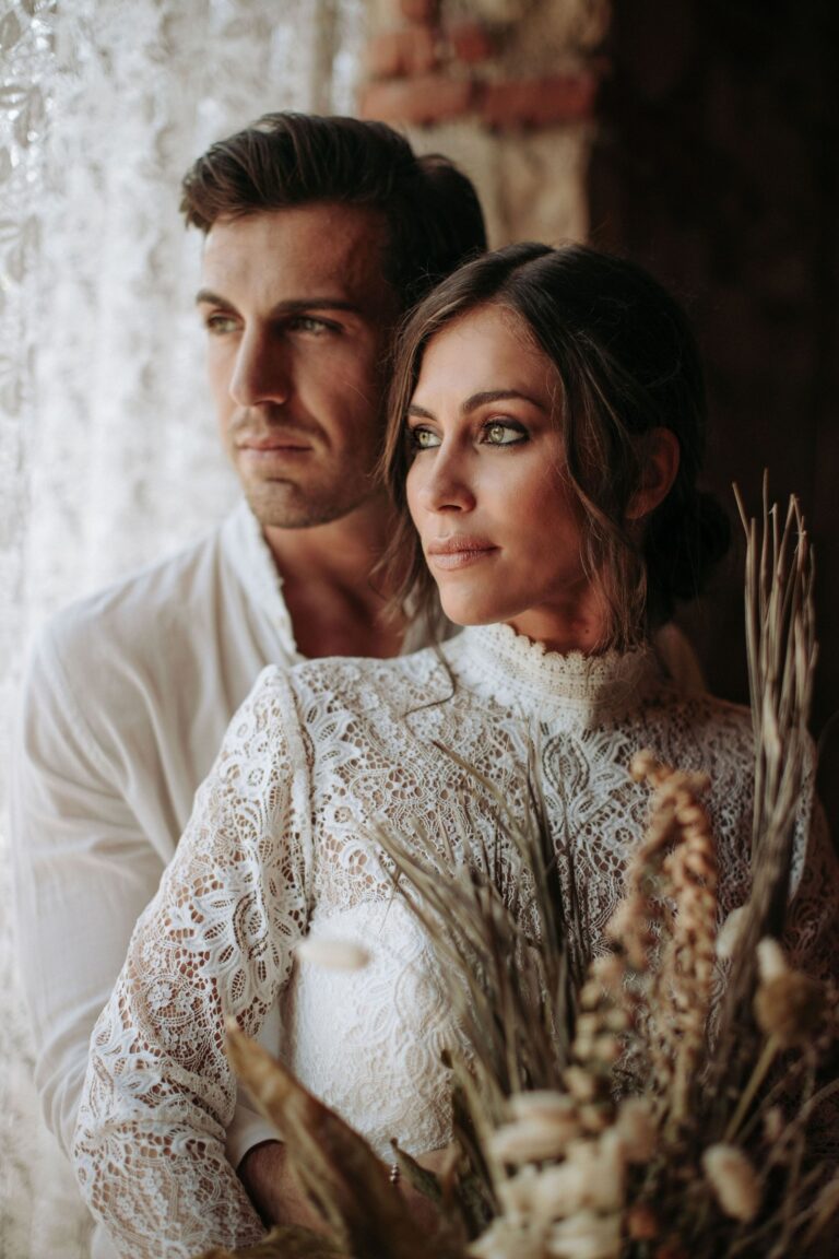 Couple in white against a pampas grass backdrop, the bride in a lace dress, Paola Giancola Makeup