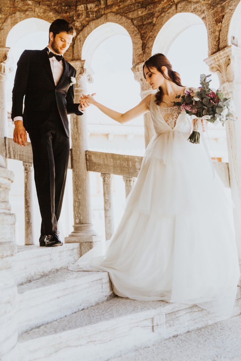 Groom and bride reaching for each other beneath the arches of a Venetian colonnade, Paola Giancola Makeup
