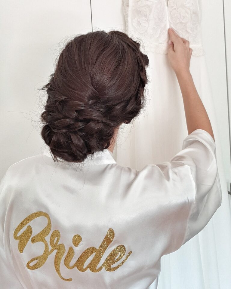 Braided bridal updo on a bride holding up her dress on a hanger, Paola Giancola Makeup