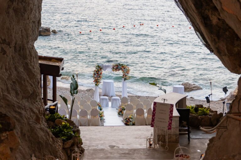 Looking out of a sea cave to a beach ceremony being set below, UNAHOTELS Capotaormina, Paola Lapi Luxury Event