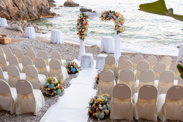 Covered chairs and a white aisle running to a floral arch on the shingle, UNAHOTELS Capotaormina, Paola Lapi Luxury Event