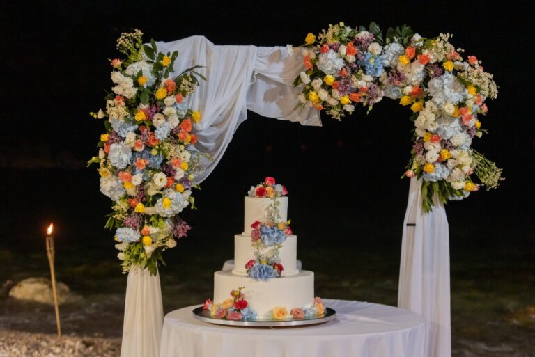 A four tier cake under the floral arch on the beach at night, UNAHOTELS Capotaormina, Paola Lapi Luxury Event