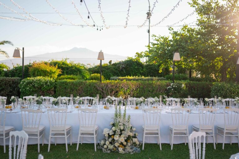 Long white tables on the lawn under strung lights, the coast on the horizon, Villa Mon Repos, Taormina, Paola Lapi Luxury Event