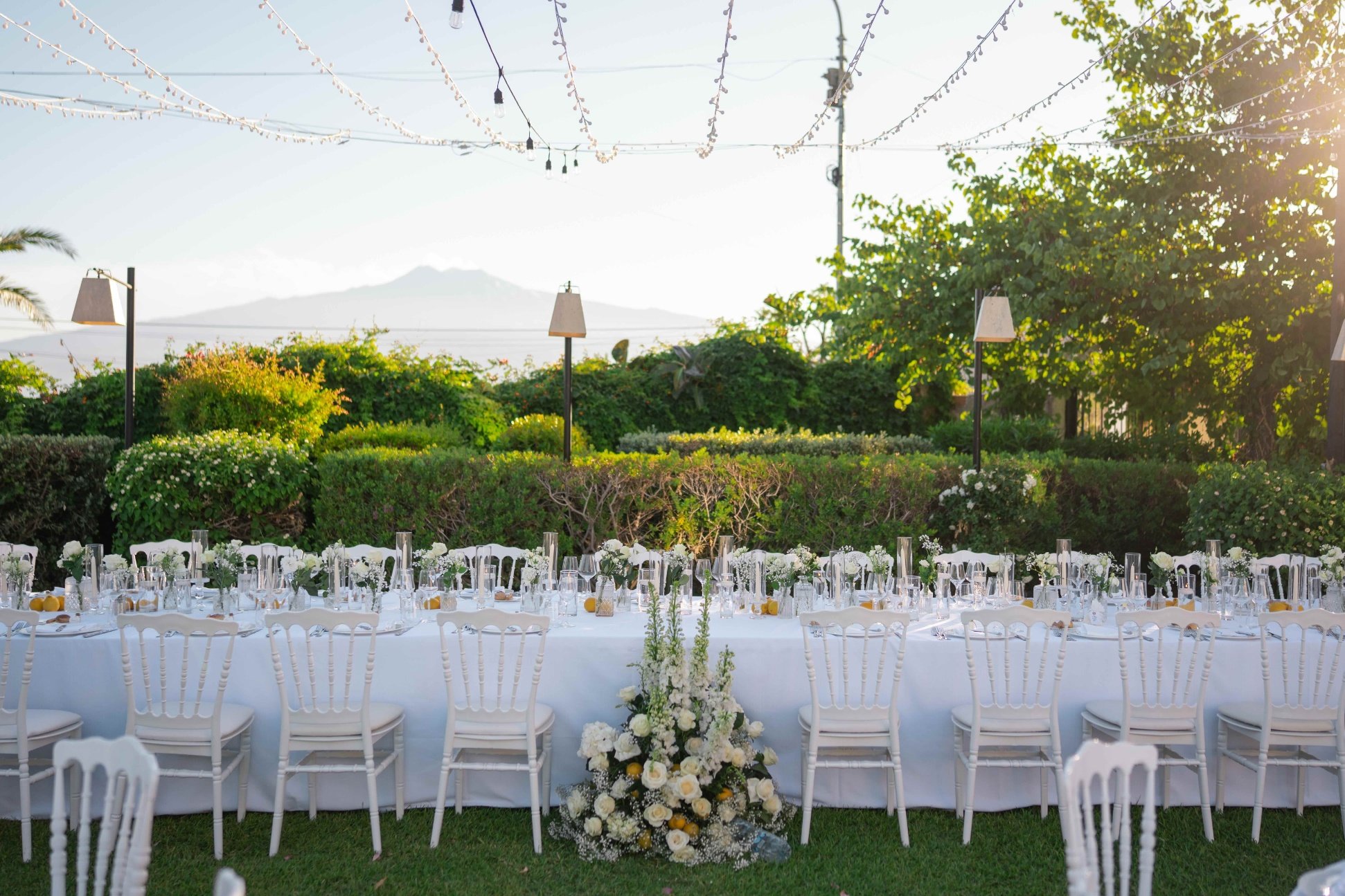 Long white tables on the lawn under strung lights, the coast on the horizon, Villa Mon Repos, Taormina, Paola Lapi Luxury Event