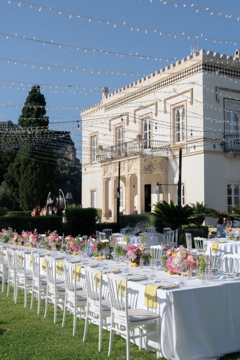 A long table with colourful flowers in front of the villa under strung lights, Villa Mon Repos, Taormina, Paola Lapi Luxury Event
