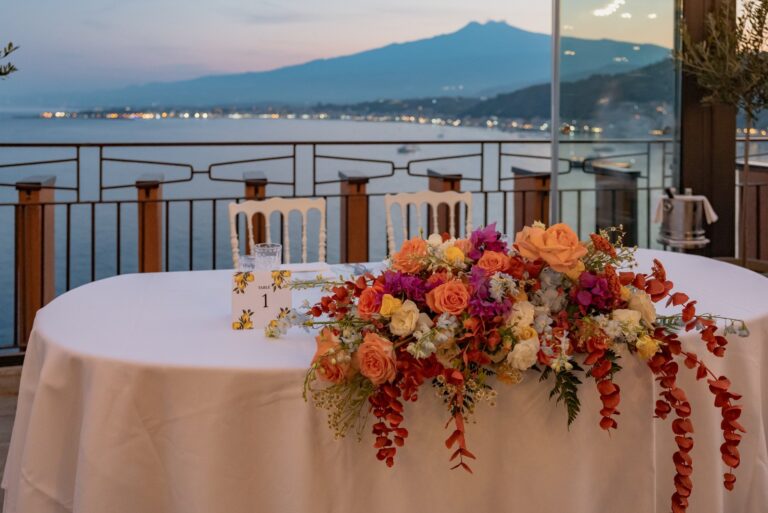 The couple's table dressed in orange and red flowers, Etna across the bay at dusk, UNAHOTELS Capotaormina, Paola Lapi Luxury Event