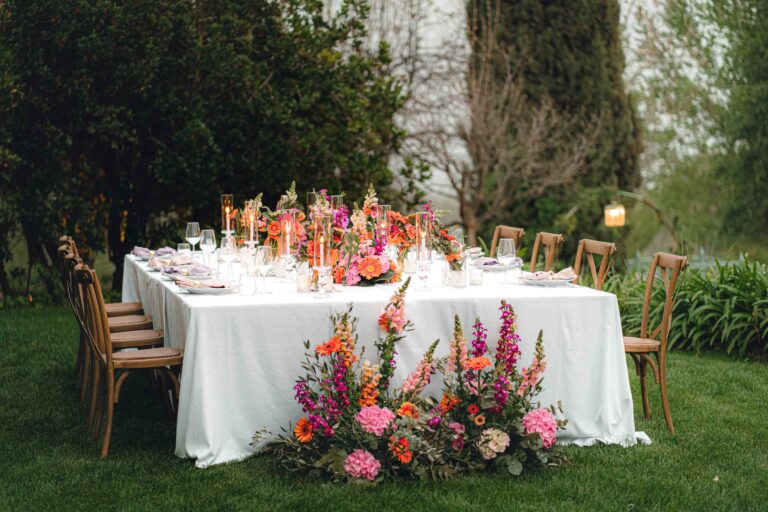 A single long table with pink and orange flowers on a garden lawn, Giardini di Villa Fago, Sicily, Paola Lapi Luxury Event
