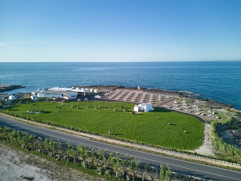 The welcome day from the air: the marquee, the parasols in rows, and open sea past the rocks, Paolo Cicognani Weddings & Events