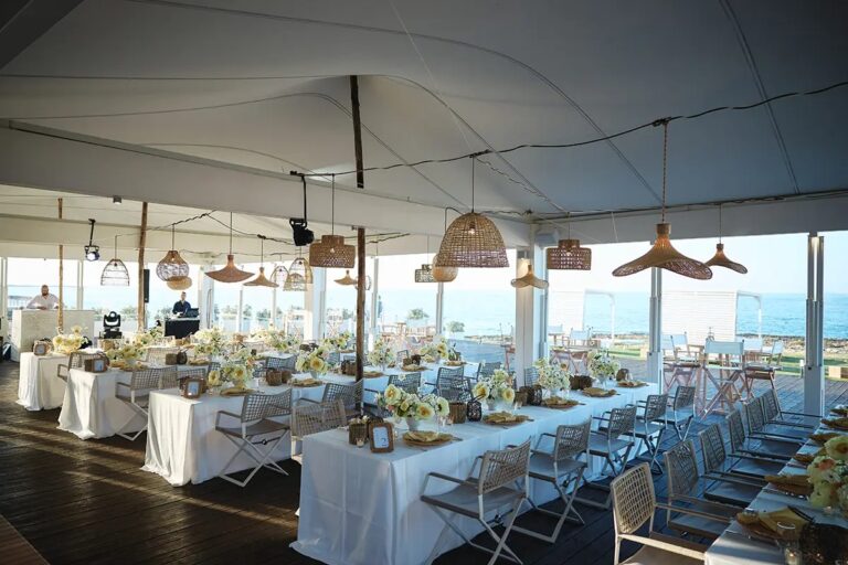 Inside the marquee: rattan pendants, white linen, and the sea through the open sides, Paolo Cicognani Weddings & Events