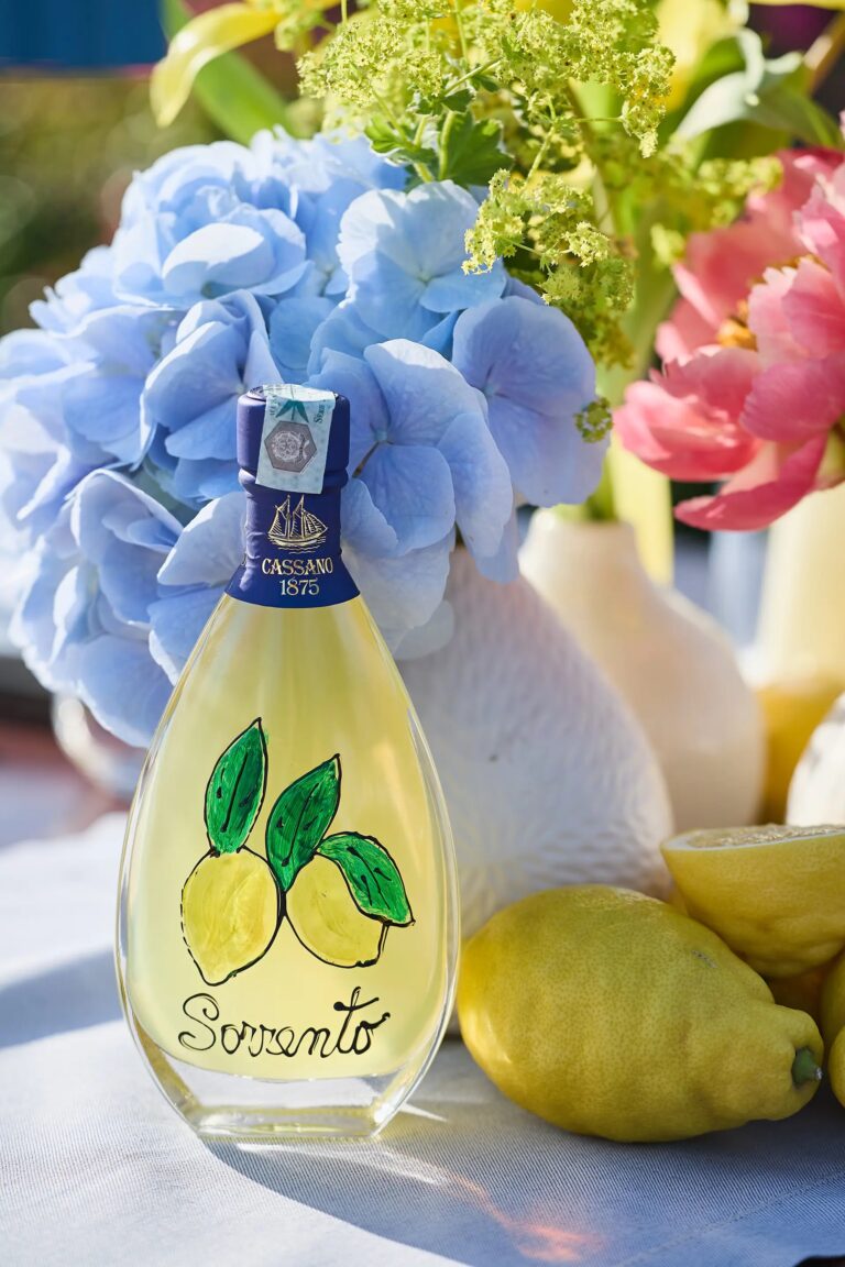 A hand-painted limoncello bottle against blue hydrangea, in full sun, Paolo Cicognani Weddings & Events