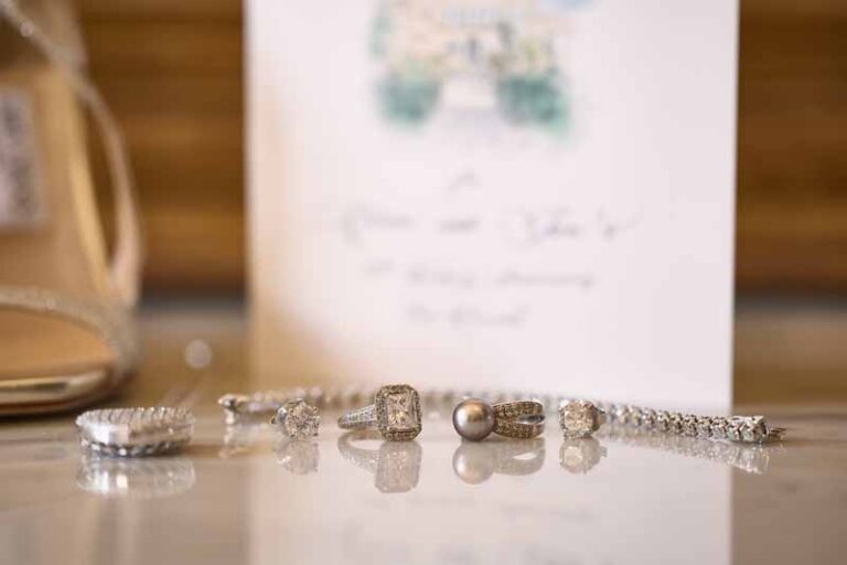 The rings and the jewellery laid out in a line on polished wood, the card behind them, Paolo Cicognani Weddings & Events