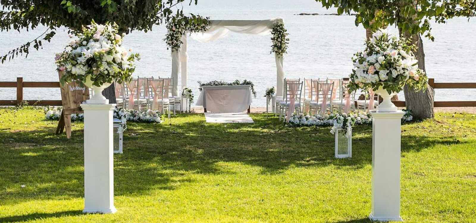 Draped canopy and white flower pedestals on the lawn beside the sea, Atlantida Beach, Paphos Weddings Made Easy