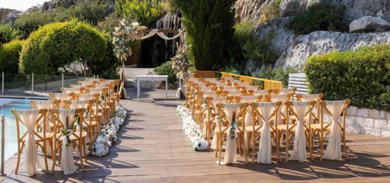 Ceremony aisle of cross-back chairs with white sashes beside the pool, Paliomonastiro, Paphos Weddings Made Easy