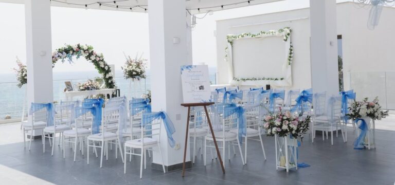 Ceremony chairs with blue sashes and a floral arch on the open sea terrace, Kefalos Beach, Paphos Weddings Made Easy