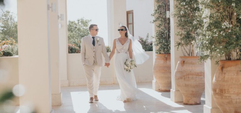 Couple walking hand in hand along a sunlit colonnade, Elea Golf Resort, Paphos Weddings Made Easy