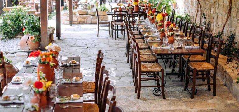 Long family-style table with bright floral arrangements on a stone terrace, Vasilias Traditional Inn, Paphos Weddings Made Easy