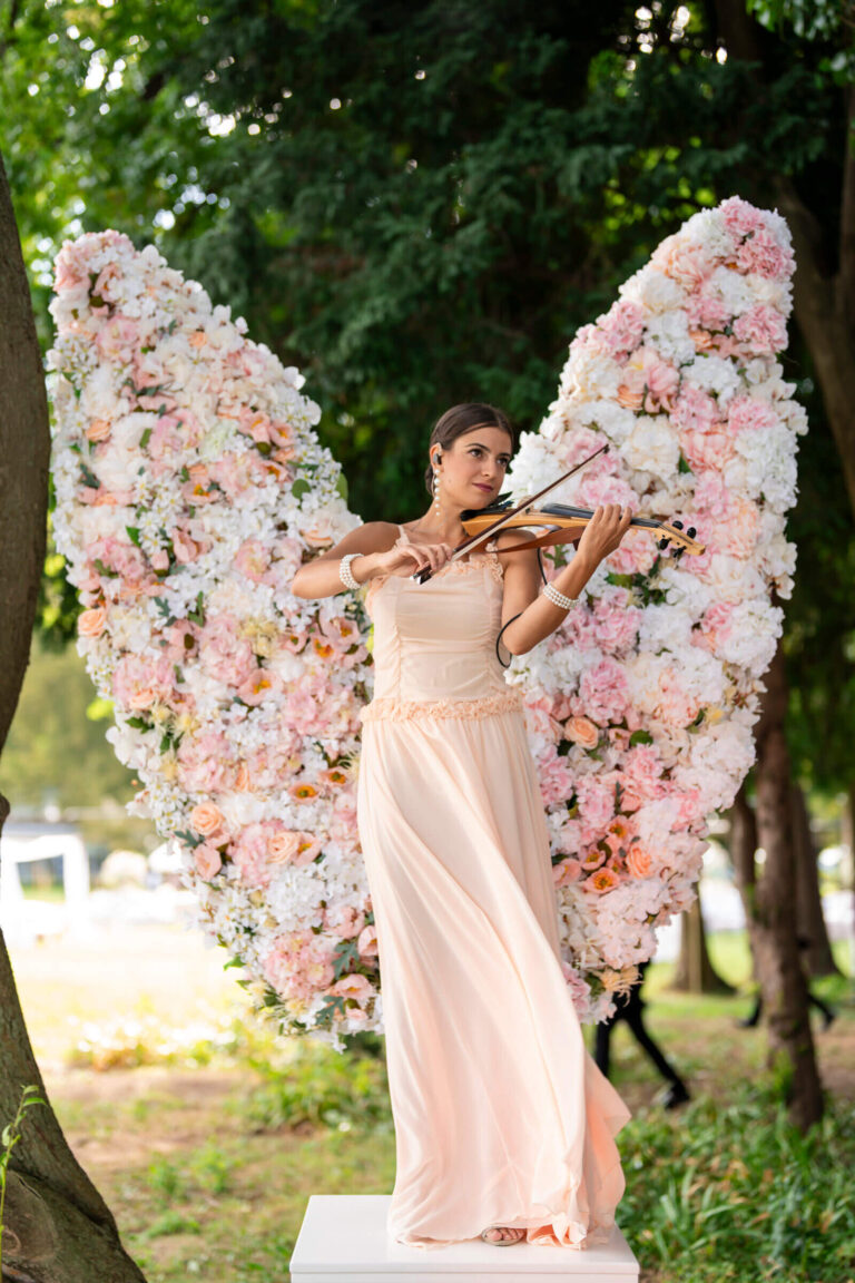Violinist in a floral angel-wing installation in a park setting, Patrizia Cilli Events Italy