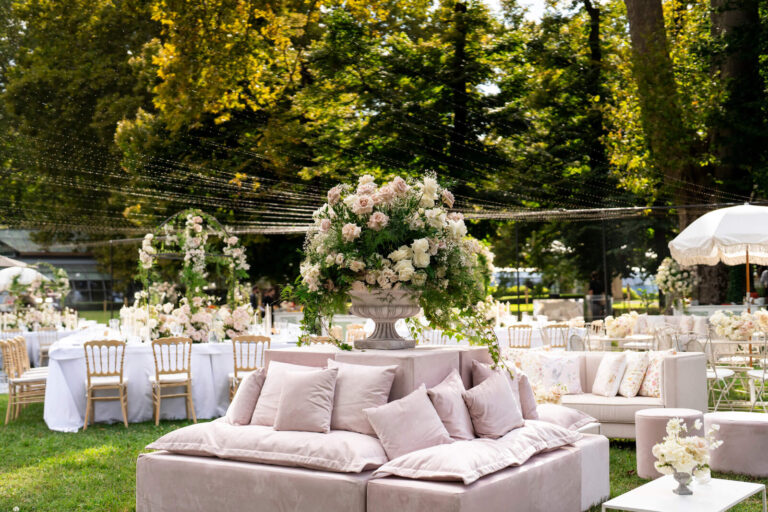 Garden lounge with cream sofas and tall floral urns under old trees, Patrizia Cilli Events Italy