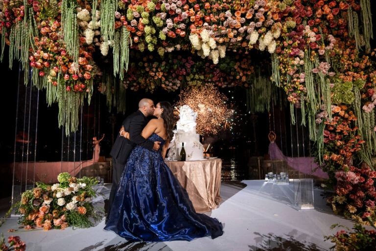 Couple embracing beneath a hanging floral canopy beside a wedding cake, Patrizia Cilli Events Italy