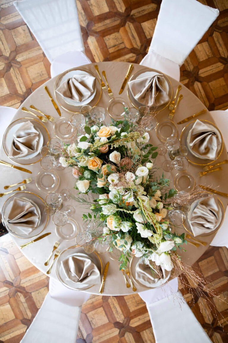 Overhead view of a round table with floral centrepiece and folded napkins on a parquet floor, Patrizia Cilli Events Italy