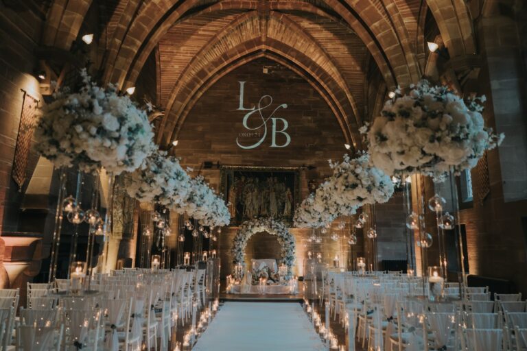 The vaulted Great Hall set for a ceremony, blue and white florals and a candle-lined aisle, Peckforton Castle