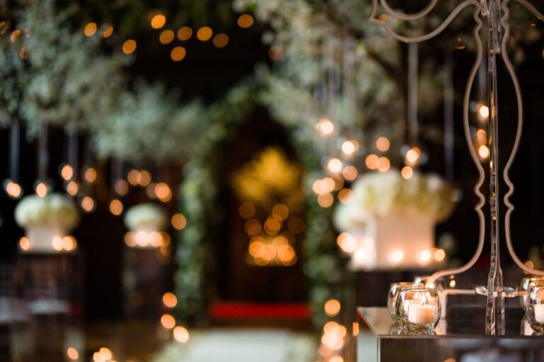 A candlelit evening reception detail, a foliage arch and glowing lights beyond, Peckforton Castle