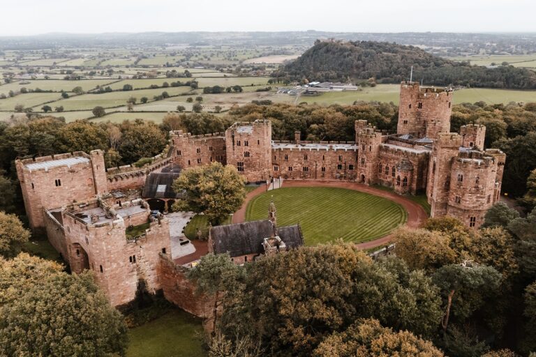 An aerial view of the whole red sandstone castle above the Cheshire plain, wrapped in autumn woodland, Peckforton Castle