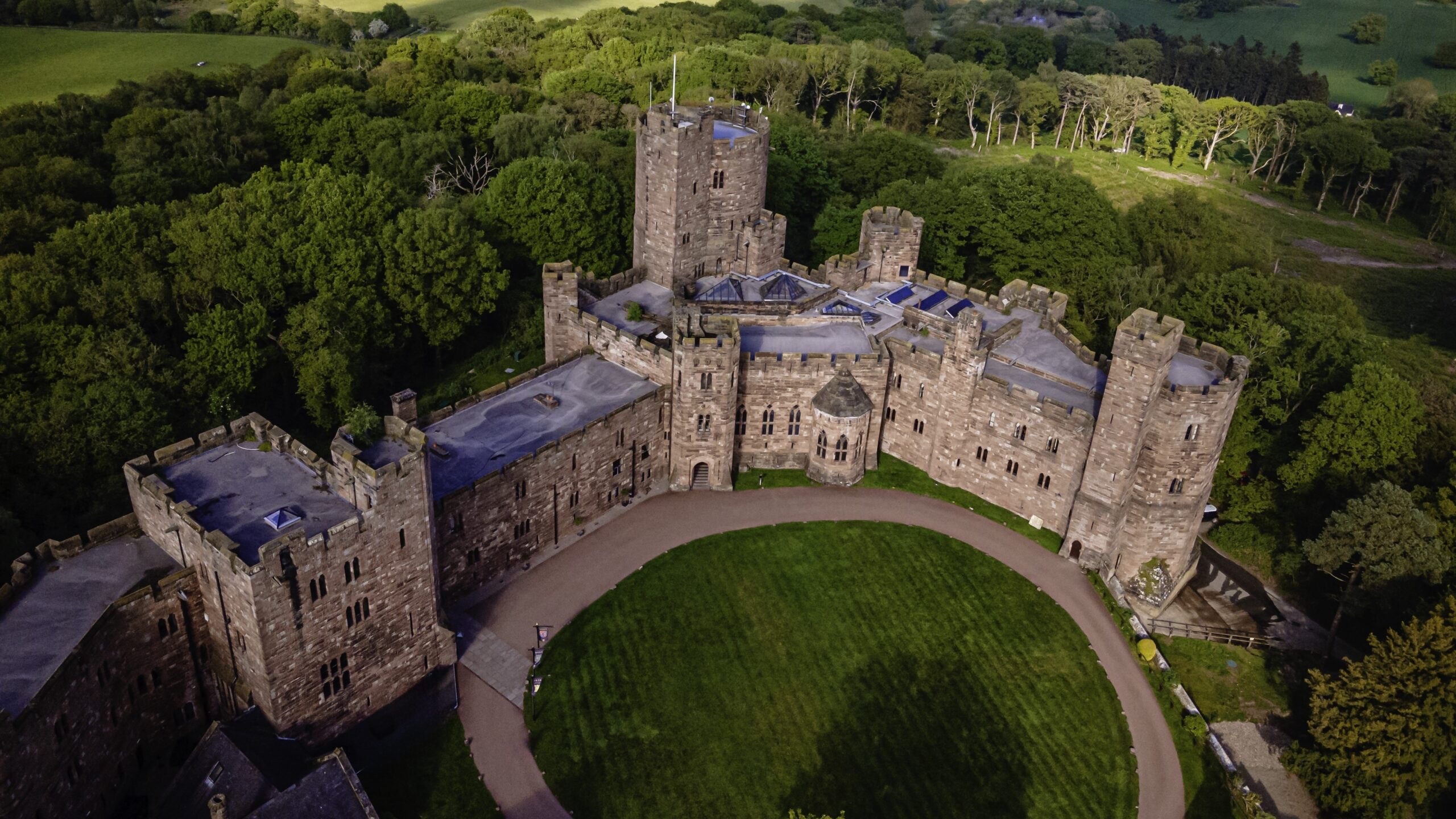 The castle from above, its inner courtyard and circular lawn ringed by towers and battlements, Peckforton Castle