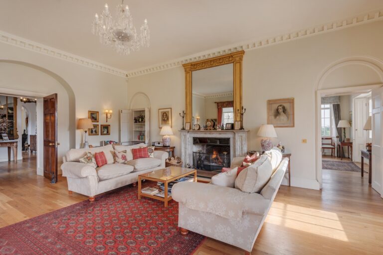 The drawing room with sofas, a fireplace and a gilt mirror, Pentillie Castle