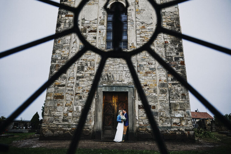 Couple at the door of a stone tower seen through ironwork, Petr Pelucha Photography