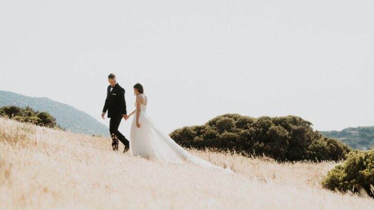 The couple walk across a dry hillside above the sea, Photomad