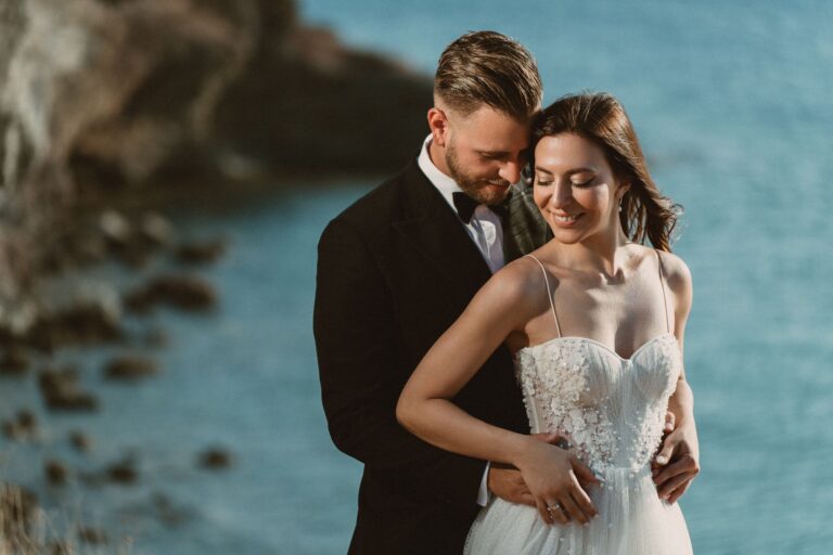 A couple embrace beside blue water, Photomad