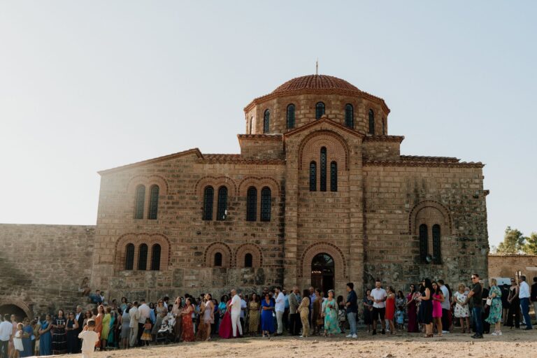 Guests gather outside a stone Byzantine style church, Photomad